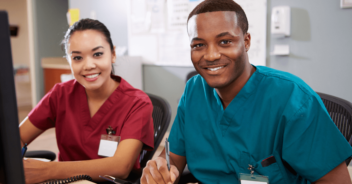 Two nurses in scrubs at a workstation on a hospital unit